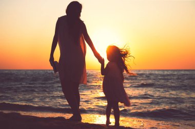 Anne ve kızı gün batımında deniz plajında birlikte oynuyor