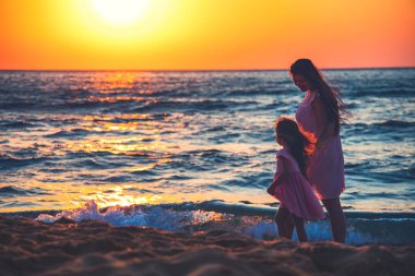 Anne ve kızı gün batımında deniz plajında birlikte oynuyor