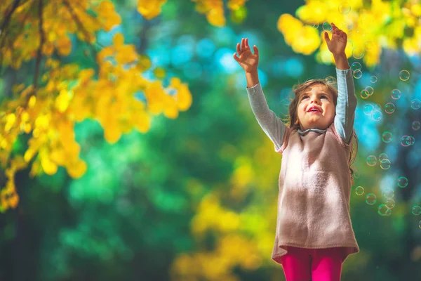 Hermosa niña jugando con hojas de árbol en un parque de otoño — Foto de Stock