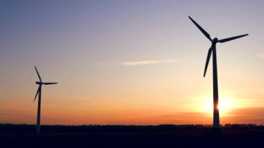 Bir tarlada günbatımında elektrik üretimi için yel değirmenleri