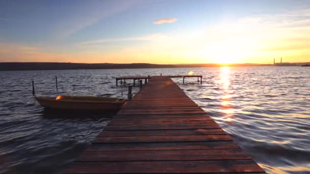 美しい日の出だ 夕暮れ時に水面に映る湖の上のボートと木製の桟橋 — ストック動画