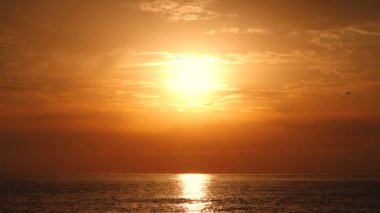 Altın gün doğumu, okyanus dalgaları üzerinde dramatik bulutlarla yanan gökyüzü.