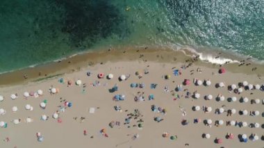 Mutlu insanlar ve plaj şemsiyeleriyle kumsal şeridi, yukarıdan deniz manzaralı.