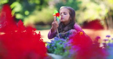 # Mutlu genç kız oynuyor ve parkta fırıldak üflüyor # # Yavaş çekimde renkli çiçeklerle #