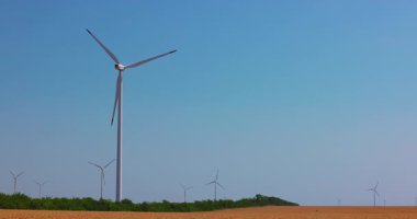 Mavi gökyüzü ve güneşe karşı dönen güç türbini, rüzgar türbini çiftliği yeşil enerji endüstrisi 4k video