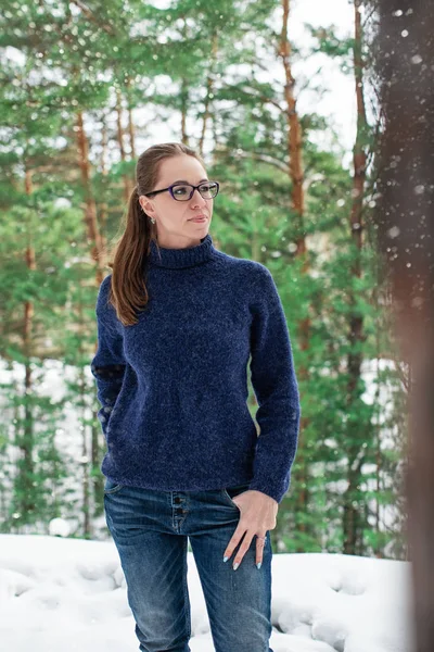 Portrait of pretty woman in a woolen blue sweater in the winter forest