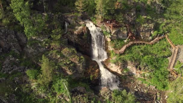 Беспилотник пролетает над зеленым лесом с водопадом в горах Алтая . — стоковое видео