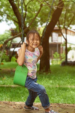 Asyalı kız kameraya bakarak bir salıncak üzerinde