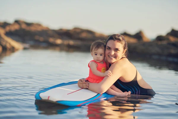 Smiling mom with baby girl on surfboard — Stock Photo, Image