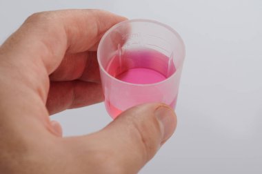 İnsan eliyle izole edilmiş pembe ilaçlı ölçü kabı.