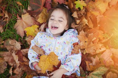 Sarı yaprak yığını içinde mutlu gülümseyen çocuk.