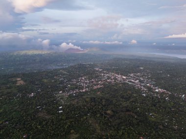 Yukarıdan bakıldığında, gün batımında çevresi dağlarla ve bulutlarla çevrili yemyeşil bir bölge görülüyor..