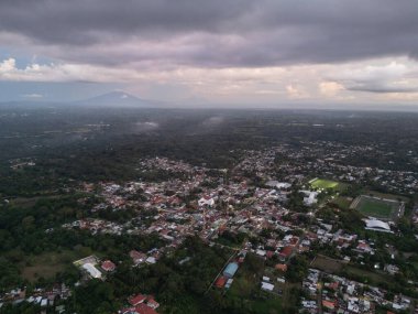 Vadide, yemyeşil yemyeşil ve bulutlu gökyüzünün altındaki uzak dağlara yuva yapmış canlı şehir manzarası..