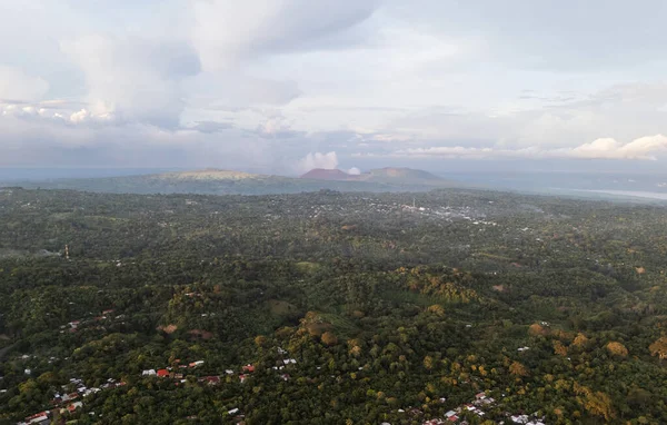 Kuş bakışı yemyeşil tepeleri ve bulutlu gökyüzünün altındaki uzak volkanik tepeleri gösterir. Doğanın günbatımındaki güzelliğini gösterir..