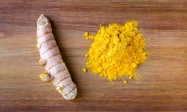 Turmeric root and spice powder on a wooden cutting board. Top view