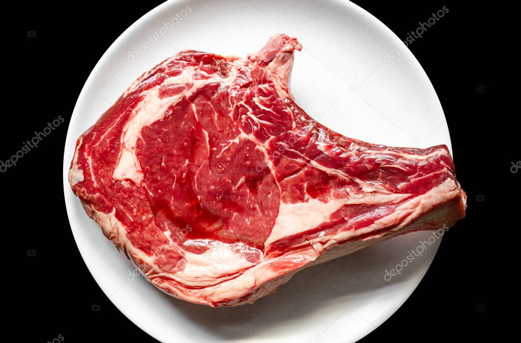 Raw beef prime rib on a plate isolated on black background. Top view
