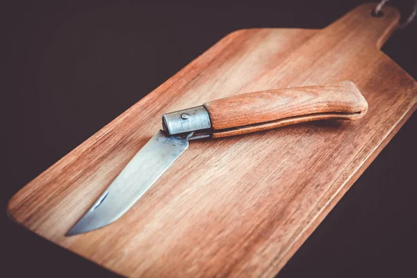 Wooden cutting board and pocket knife on a black kitchen table