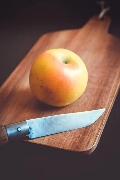 Organic fresh apple and pocket knife on a wooden cutting board