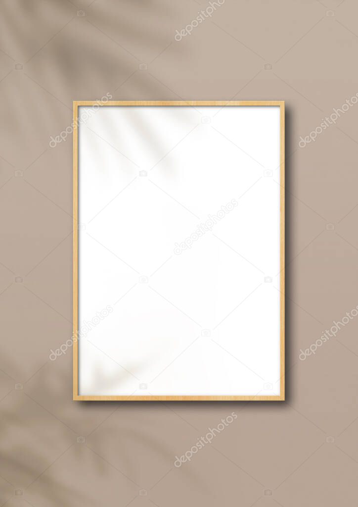 Vertical wooden picture frame hanging on a light beige wall. Floral shadows. Blank mockup template