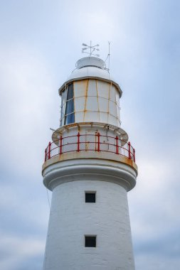 Avustralya 'daki Büyük Okyanus Yolu boyunca uzanan tarihi bir deniz feneri olan Otway Burnu bulutlu bir gökyüzüne karşı duruyor ve okyanus manzarası ve deniz tarihi sunuyor.