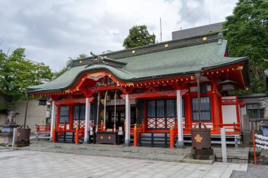 Matsumoto 'daki Fukashi-jinja Tapınağı, ağaçlar ve kentsel binalarla çevrili parlak kırmızı ahşap döşeme, kıvrımlı çatı hatları ve geleneksel motiflerle dekore ediliyor.