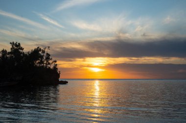 Altın gün batımı ışığı, Lia Sahili, Waleakodi Adası, Togian takımadası, Sulawesi, Endonezya 'daki sakin denizi yansıtarak, barışçıl bir tropik manzara yaratır.