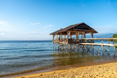 Sazdan kulübesi olan ahşap bir iskele, Sulawesi, Tentena 'da kumlu bir sahil boyunca Poso Gölü' nün sakin suları üzerine uzanır.