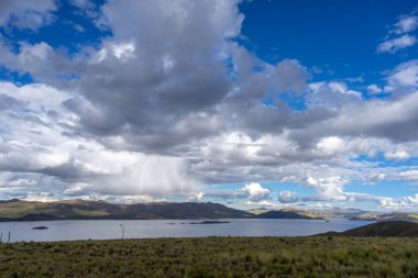 Peru 'daki Lagunillas Gölü, üzerinde kara fırtına bulutları ve dağların üzerine yağan yağmur yağmuru ile yuvarlanan tepeler ve otlaklarla çevrilidir.