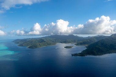 Fransız Polinezyası 'ndaki Tahaa adası, yukarıdan bakıldığında turkuaz bir göl, mercan resifi ve yemyeşil dağları ortaya çıkarır. Canlı okyanus renkleri koyu mavi Pasifik ile tezat oluşturuyor.