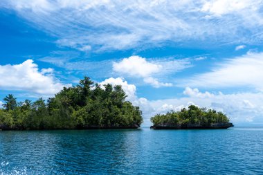 Togian Adaları, Sulawesi, Endonezya 'daki bulutlarla dolu gökyüzünün altındaki derin mavi sulardan küçük orman adaları yükselir.