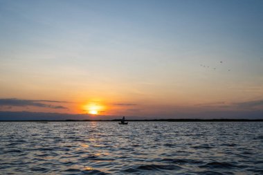 Gün batımında Tempe Gölü 'nde süzülen küçük bir tekne, Endonezya, Sulawesi' nin huzurlu sularına yansıyan altın gökyüzü.