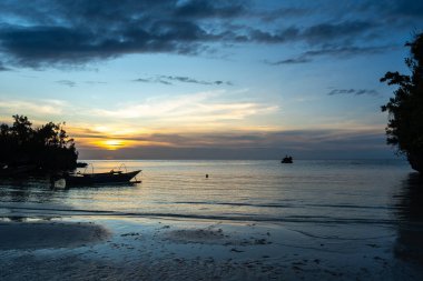 Geleneksel bir pirogue, Waleakodi Adası, Togian takımadaları, Sulawesi, Endonezya 'daki renkli bir günbatımında Lia Sahili' nin yumuşak kumlarına dayanır.