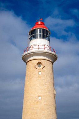 Cape Du Couedic deniz feneri Avustralya 'nın Kanguru Adası' ndaki Flinders Chase Ulusal Parkı 'nda kıyı bitkilerinin arasında yer alır. Kırmızı ve beyaz tepesi bulutlu gökyüzü ile çelişiyor.