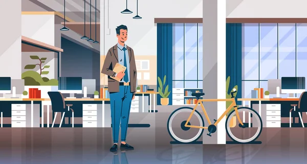 Empresário segurando laptop criativo escritório co-working centro quarto interior moderno local de trabalho mesa bicicleta ecológico transporte horizontal completo comprimento plano —  Vetores de Stock