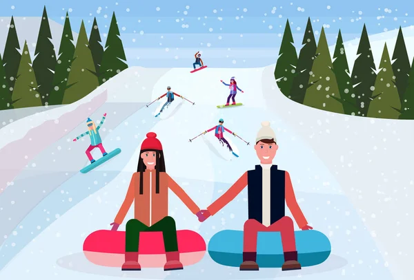 couple sledding on snow rubber tube over snowboarders skiers people sliding down snowy mountain hill fir tree landscape background winter vacation concept flat horizontal