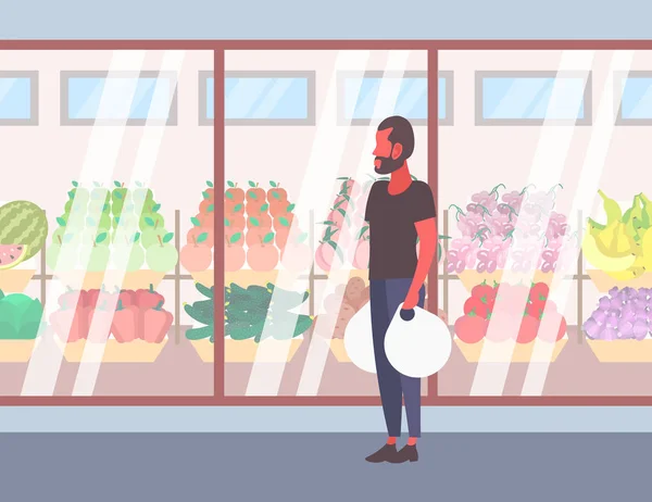 Homme décontracté tenant des sacs à provisions marchant devant des fruits biologiques frais légumes moderne supermarché magasin verre fenêtre gars client pleine longueur personnage de dessin animé plat — Image vectorielle
