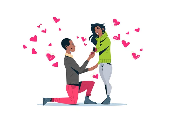 Muž klečí drží zásnubní prsten navrhuje žena si ho šťastný valentines den koncept afroamerické pár v láska manželství nabídka růžové srdce obrazce vodorovného izolované — Stockový vektor