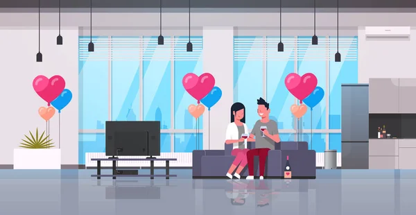 Pareja beber vino hombre mujer amantes viendo tv en sofá moderno apartamento casa interior aire forma corazón globos feliz día de San Valentín concepto plano horizontal — Vector de stock