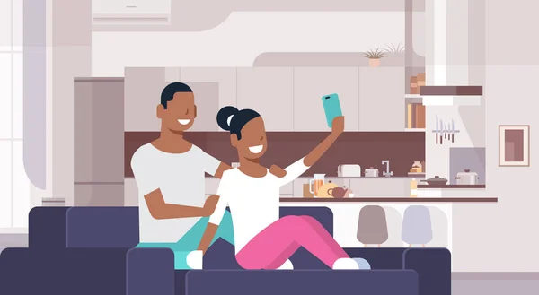 Pareja tomando foto selfie en el teléfono inteligente hombre afroamericano mujer sentada en el sofá jóvenes amantes felices cocina moderna interior masculino personajes de dibujos animados femeninos plana horizontal — Vector de stock