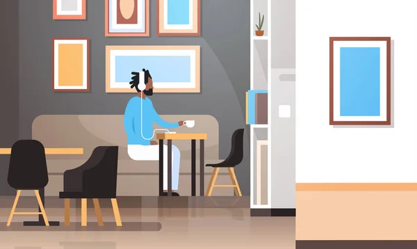 Homem bebendo café ouvindo música no smartphone com fones de ouvido afro-americano hipster cara sentado à mesa moderno café interior plana horizontal comprimento total — Vetor de Stock