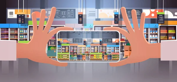 Mano humana celebración de teléfono inteligente tomar foto interior moderno supermercado con surtido de alimentos de alimentación que se muestra en la pantalla del teléfono móvil plana horizontal — Archivo Imágenes Vectoriales