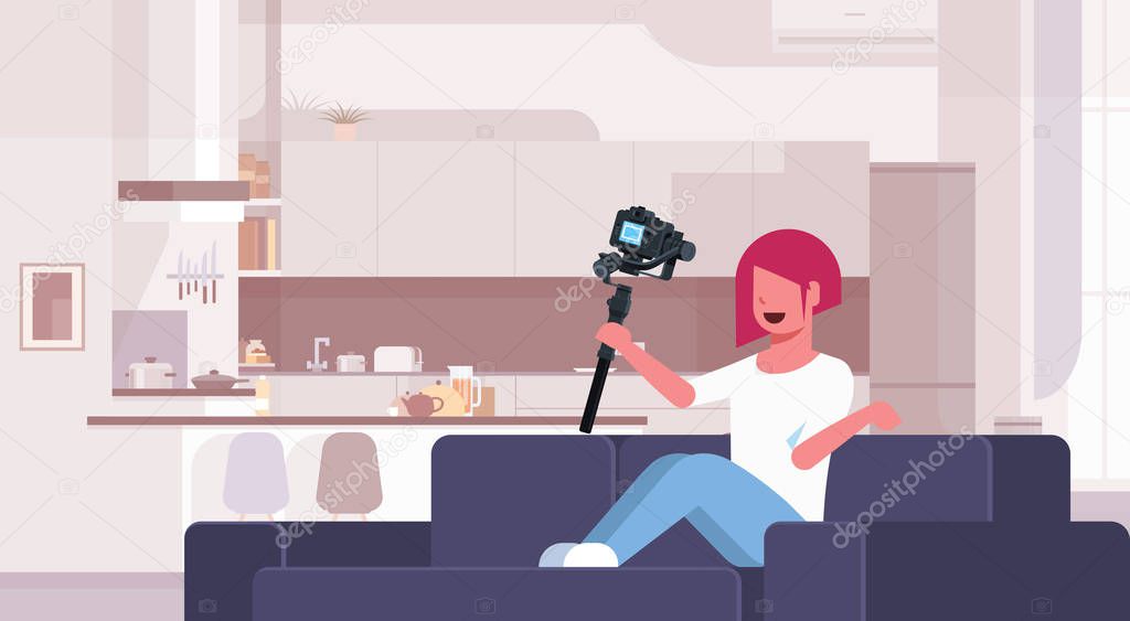girl blogger recording video on camera woman sitting on couch modern kitchen interior using motorized gimbal stabilizer social media blog concept full length flat horizontal