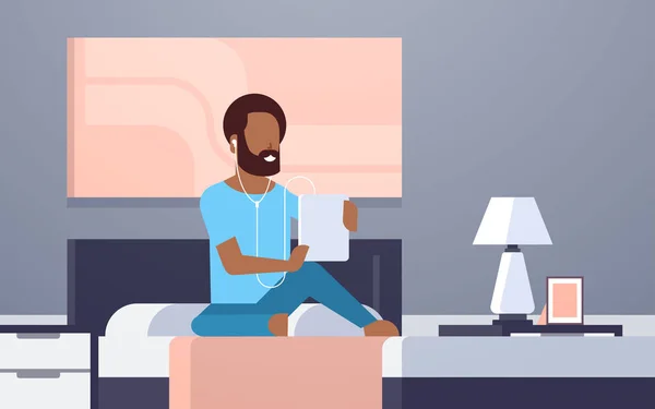 Hombre escuchar audio libro a través de auriculares afroamericano chico usando tableta sentado en la cama moderna casa dormitorio interior masculino carácter longitud completa plana horizontal — Vector de stock