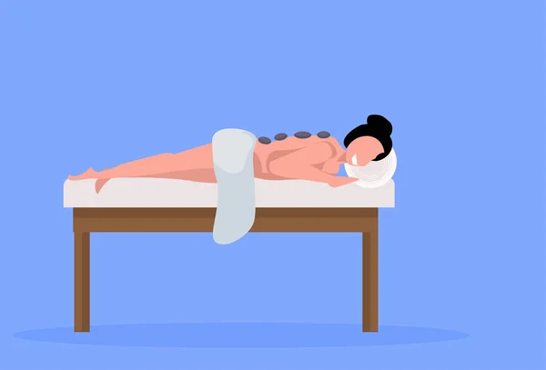 Jeune fille client appréciant traditionnelle pierre chaude massage patient femme couché sur le lit luxe spa et centre de bien-être concept horizontal pleine longueur fond bleu — Image vectorielle