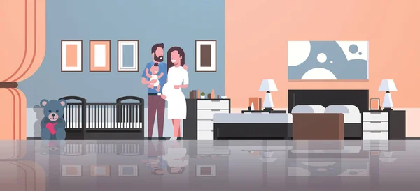 Marido con embarazo esposa sosteniendo bebé recién nacido hijo de pie cerca de cuna feliz familia paternidad concepto moderno hogar dormitorio interior piso de longitud completa — Archivo Imágenes Vectoriales