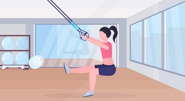 Elastik ipi kız eğitim crossfit egzersiz kavramı modern bir spor salonu studio iç yatay düz tam uzunlukta sportif kadın ile süspansiyon fitness egzersizleri yapıyor kayışlar