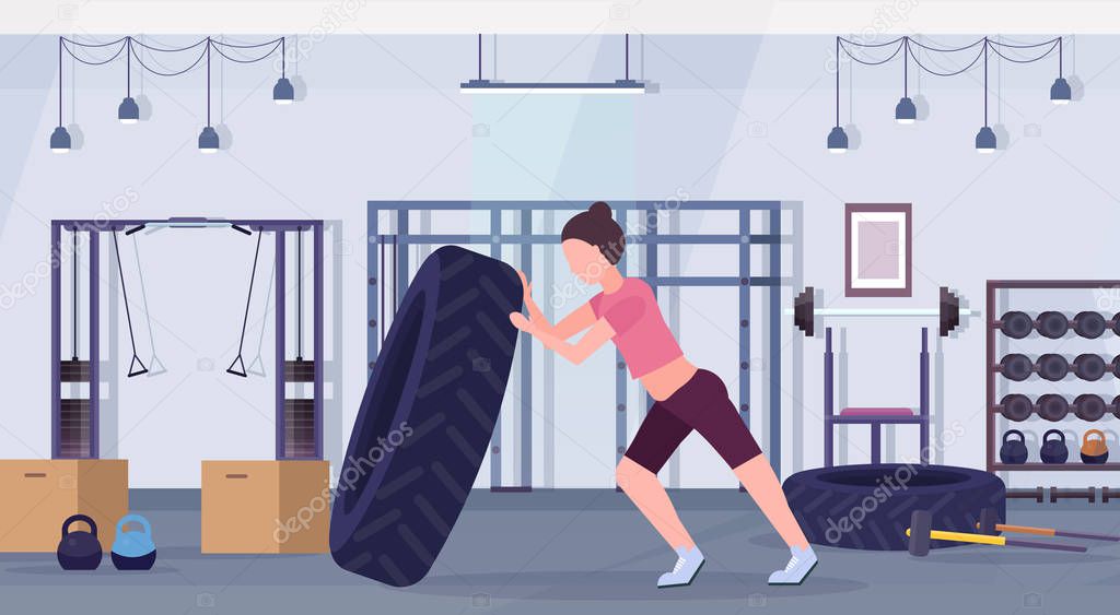 sports woman flipping a tire doing hard exercises girl working out in gym crossfit training healthy lifestyle concept modern health club studio interior horizontal