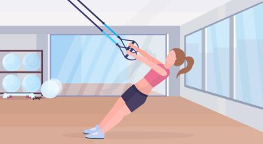 Elastik ipi kız eğitim crossfit egzersiz kavramı modern bir spor salonu studio iç yatay düz tam uzunlukta sportif kadın ile süspansiyon fitness egzersizleri yapıyor kayışlar
