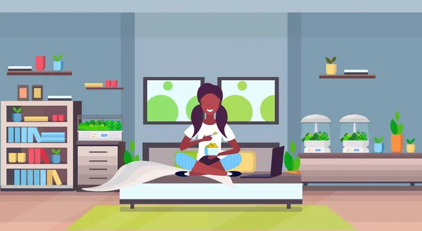 Menina africana sentado na cama comendo frutas frescas salada apartamento moderno quarto interior com casa eletrônica terrário vidro recipiente casa plantas crescente conceito plana horizontal — Vetor de Stock