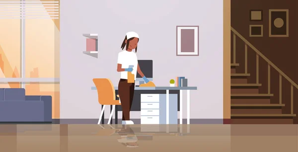 Housewife cleaning computer table with duster african american woman wiping workplace desk housework concept modern living room interior female cartoon character full length horizontal — Stock Vector